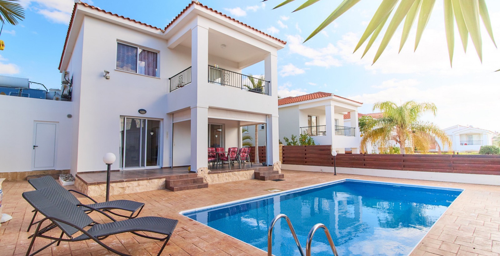 Pool at Villa Natalia, with a metal ladder, sun loungers and a covered outdoor dining area beside the house.